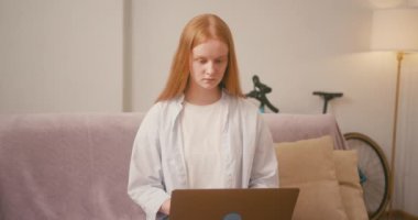 Laptopta oturan kızıl saçlı kadınlar koltukta rahatça otururlar. Bayan, rahat ev ortamları arasında tereddütsüz serbest yöneticilik işine odaklanıyor