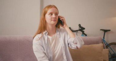 Kızıl saçlı kadın telefonuna sıcak bir gülümsemeyle cevap veriyor. Bayan tatlı ve büyüleyici bir diyalog kuruyor arayanla sıcak bir bağ kuruyor.