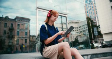 Tabletli ve dışarıda kırmızı kulaklıklı güzel bir bayan öğrenci. Şehir caddesinde üniversite öğrencisi..