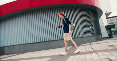 Sırt çantası ve açık havada telefonla dans eden güzel bir kız öğrenci. Üniversite öğrencisi kampüste mutlu..