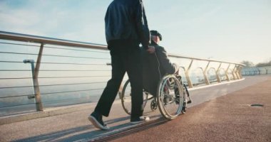 İspanyol adam tekerlekli sandalyedeki engelli arkadaşla ilgileniyor. Arkadaşlar sonbahar parkında birlikte vakit geçiriyorlar. Sağlık, sakatlık, hareketlilik, arkadaşlık.