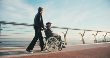 İspanyol adam tekerlekli sandalyedeki engelli arkadaşla ilgileniyor. Arkadaşlar sonbahar parkında birlikte vakit geçiriyorlar. Sağlık, sakatlık, hareketlilik, arkadaşlık.