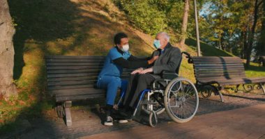 İspanyol doktor tekerlekli sandalyedeki engelli arkadaşla ilgileniyor. Latin sıhhiyeci, yaşlı adama sonbahar parkında rehabilitasyonda yardım ediyor. Sağlık, sakatlık, hareketlilik, arkadaşlık.