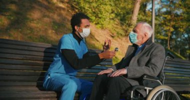 İspanyol doktor tekerlekli sandalyedeki engelli arkadaşla ilgileniyor. Latin sıhhiyeci, yaşlı adama sonbahar parkında rehabilitasyonda yardım ediyor. Sağlık, sakatlık, hareketlilik, arkadaşlık.