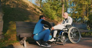 İspanyol doktor tekerlekli sandalyedeki engelli arkadaşla ilgileniyor. Latin sıhhiyeci, yaşlı adama sonbahar parkında rehabilitasyonda yardım ediyor. Sağlık, sakatlık, hareketlilik, arkadaşlık.