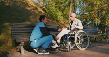 İspanyol doktor tekerlekli sandalyedeki engelli arkadaşla ilgileniyor. Latin sıhhiyeci, yaşlı adama sonbahar parkında rehabilitasyonda yardım ediyor. Sağlık, sakatlık, hareketlilik, arkadaşlık.