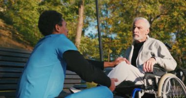 İspanyol doktor tekerlekli sandalyedeki engelli arkadaşla ilgileniyor. Latin sıhhiyeci, yaşlı adama sonbahar parkında rehabilitasyonda yardım ediyor. Sağlık, sakatlık, hareketlilik, arkadaşlık.