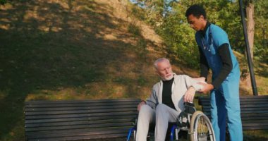İspanyol doktor tekerlekli sandalyedeki engelli arkadaşla ilgileniyor. Latin sıhhiyeci, yaşlı adama sonbahar parkında rehabilitasyonda yardım ediyor. Sağlık, sakatlık, hareketlilik, arkadaşlık.
