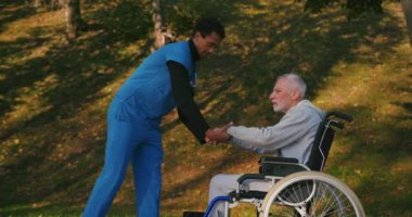 İspanyol doktor tekerlekli sandalyedeki engelli arkadaşla ilgileniyor. Latin sıhhiyeci, yaşlı adama sonbahar parkında rehabilitasyonda yardım ediyor. Sağlık, sakatlık, hareketlilik, arkadaşlık.