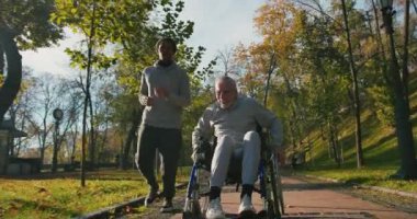 İspanyol adam tekerlekli sandalyedeki engelli arkadaşla ilgileniyor. Sonbahar parkında birlikte eğlenen arkadaşlar. Sağlık, sakatlık, hareketlilik, arkadaşlık.