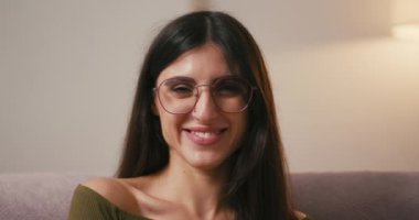 İspanyol kadın evde sevgi dolu kalp hareketleri göstererek gülüyor. Genç bayan oturma odasındaki rahat kanepede oturarak mutluluğun tadını çıkarıyor.