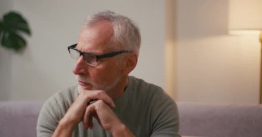 Endişeli yetişkin adam oturma odasındaki kanepede oturan gözlükleri çıkartıyor. Gri saçlı yaşlı Arap erkek derin iç geçiriyor olumsuz duygular yaşıyor.