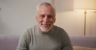 Mutlu, olgun bir adam evdeki koltukta oturmaktan zevk alan yumruklarını sıkar. Yaşlı Arap erkek, gri sakallı. Televizyon izlemekten memnun.