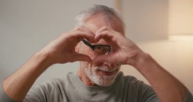 Gözlüklü olgun bir Arap, elleri öptüğünde kalbi şekillendirir. Neşeli, gri saçlı, yaşlı erkek oyuncu hareketlerle aşkı ifade eder.