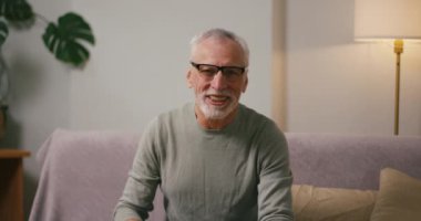 Mutlu kıdemli adam evdeki blog için el sallıyor. Gri saçlı olgun Arap erkek blogcu gözlüklü eğlence içeriği yaratıyor