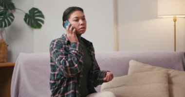 Günlük kıyafetli ciddi bir İspanyol kadın oturma odasındaki akıllı telefondan durumu açıklıyor. Esmer kadın cep telefonuyla konuşuyor.