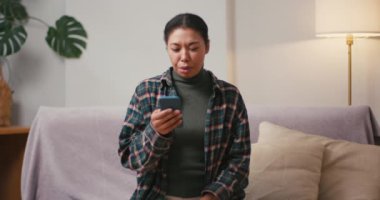 İspanyol kadın, oturma odasındaki akıllı telefondan gelen kötü haberle ağlar. Üzgün kadın evdeki cep telefonundan keder e-postası okuduğunu söylüyor.