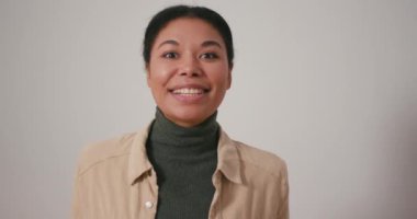 Heyecanlı Latin Amerikalı kadın arka planda mutlu bir şekilde el kol hareketi yapıyor. Genç esmer kadın video aracılığıyla arkadaşlarına etkileyici haberler veriyor.