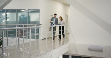 İş adamları, üst kattaki ofis geçidi boyunca yürüme projesini tartıştılar. Kadın ve erkek iş belgelerini ellerinde tutarak iletişim kurarlar.