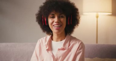 Kablosuz kulaklıklı Latin kadın evdeki kanepede oturmuş video konuşmalarıyla konuşuyor. Sapık saçlı genç bir kadın en iyi arkadaşıyla iletişim kuruyor.