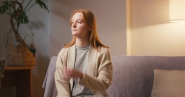 Endişeli kadın oturma odasında kanepede oturarak kollarını kavuşturuyor. Kızıl saçlı genç bayan akşamları duygusal gerilim yaşıyor.