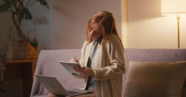 Dizüstü bilgisayarı olan bir kadın akıllı telefondan konuşur ve notlar alır. Genç kızıl saçlı kadın, akşam evde meslektaşlarıyla birlikte iş çözme işine girişiyor.