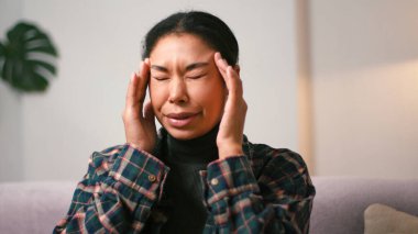 Genç İspanyol kadın evde beklenmedik migren kriziyle baş etmek için tapınaklara masaj yapıyor. Kanepede oturan kadın baş ağrısından muzdarip.