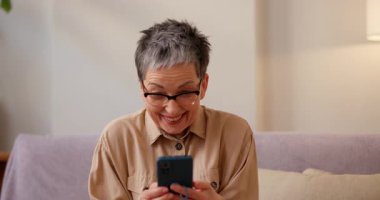 Gözlüklü Latin kadın sosyal medyada yazı okuyor ve gülüyor. Son sınıf öğrencisi bayan akıllı telefondan esprili mesajlar okuyor ve kanepede kahkahalarla gülüyor.