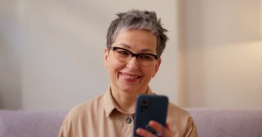 İspanyol kadın akıllı telefonu tutuyor ve selamla el sallamaya başlıyor. Son sınıf öğrencisi kadın rahat bir şekilde kanepede oturuyor ve en iyi arkadaşıyla konuşuyor.