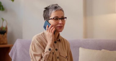 Gözlüklü İspanyol kadın, kızıyla son seyahati konuşmak için akıllı telefon kullanıyor. Kıdemli bayan mutlu bir şekilde gülümsüyor ve neşeli sohbetlerden hoşlanıyor.