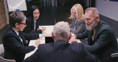 Masada oturan çeşitli iş adamları beyin fırtınası fikirleri. Erkekler ve kadınlar modern ofiste stratejik yönetim kurulu toplantısında görüşlerini paylaşıyorlar.