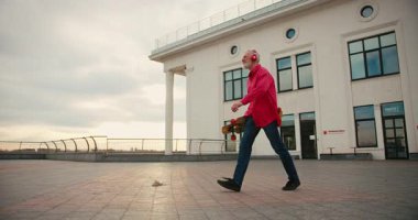 Aktif, mutlu, yaşlı, kırmızı tişörtlü kaykaycı gün batımından sonra şehir merkezinde kaykayla geziyor. Yaşlılar özgürlük ruhu kavramı. Yavaş çekim.