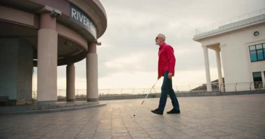 Beyaz bastonlu yaşlı kör adam caddede yürüyor. Engellilik ve şehir keşfi