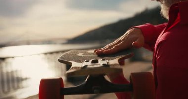 Aktif, mutlu, yaşlı kaykaycı kırmızı tişörtlü şehir merkezinde gün batımında kaykaya biniyor. Yaşlılar özgürlük ruhu kavramı. Yavaş çekim.