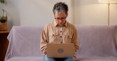 Yorgun İspanyol kadın evde dizüstü bilgisayarla çalışırken boynuna masaj yapıyor. Üst düzey bayan aşırı yüklenen online görevlerle ilgili yorgunluk belirtileri gösteriyor.
