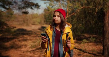 Sırt çantalı gezgin kız yürüyüş direkleri ile akıllı telefondaki harita uygulamasını kullanarak rota bulmak için