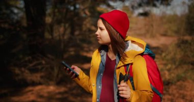 Sırt çantalı gezgin kız yürüyüş direkleri ile akıllı telefondaki harita uygulamasını kullanarak rota bulmak için