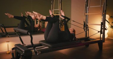 Siyah tulumlu kadın pilates egzersizi yapıyor göğüs ve sırt kasları için reformist, esneklik, güç ve kararlılıkla kontrol üzerine odaklanıyor.