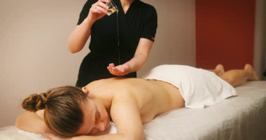 Spa Salonu 'nda yatakta uzanan ve masajdan zevk alan mutlu genç kadın. Kozmetikçi, lenfatik drenaj ve kaldırma efekti için kadın müşteriye masaj yağı döktü. Güzellik, Cilt Bakımı.