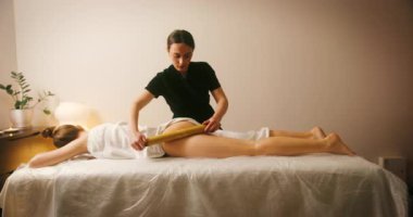 Spa Salonu 'nda yatakta uzanan ve Creole Sticks masajının tadını çıkaran mutlu genç kadın. Lenfatik drenaj ve kaldırma efekti için kozmetik uzmanı kadın müşteriye masaj yapıyor. Güzellik, Cilt Bakımı.