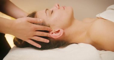 Spa Salonu 'nda yatakta uzanan ve yüz masajından zevk alan mutlu genç kadın. Lenfatik drenaj ve kaldırma efekti için kadın müşteri yüzüne masaj yapan kozmetik uzmanı. Güzellik, Cilt Bakımı.