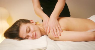 Spa Salonu 'nda yatakta uzanan ve sırt masajının tadını çıkaran mutlu genç kadın. Lenfatik drenaj ve kaldırma efekti için Kadın Müşteri Sırtına ve Boynuna Masaj Yapan Kozmetolog. Güzellik, Cilt Bakımı.