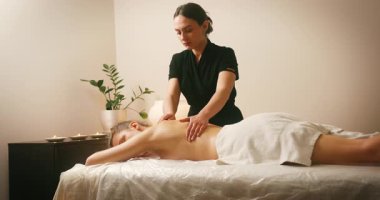 Spa Salonu 'nda yatakta uzanan ve sırt masajının tadını çıkaran mutlu genç kadın. Lenfatik drenaj ve kaldırma efekti için Kadın Müşteri Sırtına ve Boynuna Masaj Yapan Kozmetolog. Güzellik, Cilt Bakımı.