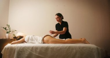 Spa Salonu 'nda yatakta uzanan ve masajdan zevk alan mutlu genç kadın. Kozmetikçi, lenfatik drenaj ve kaldırma efekti için kadın müşteriye masaj yağı döktü. Güzellik, Cilt Bakımı.