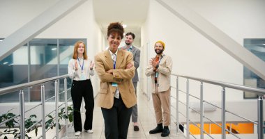 Farklı meslektaşları koridorda alkışlarken melez bir kadın kollarını kavuşturarak ayakta duruyor. İşçiler takım üyesinin başarısını kutladılar