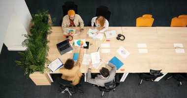 Çeşitli profesyoneller modern ofisteki belgeleri incelemek için konferans masasına otururlar. İş adamları toplantıda mali performansı analiz ediyor