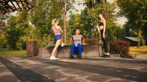 Bayan sporcular sabah parkta antrenman yapmak için bacaklarını esnetiyorlar. Spor kadınları şehir bahçesinin huzurlu ortamlarında birlikte ısınırlar. Yavaş çekim