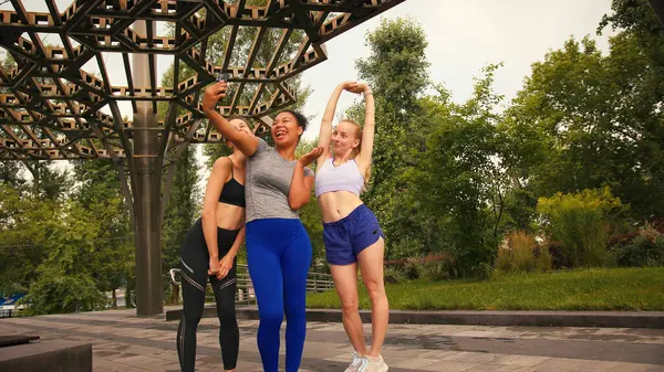 Bayan sporcular birbirine yakın durur ve kenar mahallelerde selfie çekerken gülümserler. Spor kadınları neşeli grup fotoğrafları çekmek için akıllı telefon kullanır. Yavaş çekim