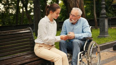 Genç bir kadın ve yaşlı bir adam parkta bankta oturmuş akıllı telefona bakıyor ve konuşuyorlar. Ortak ilgi ve bağlantı, nesiller arası boşlukları oluşturur.