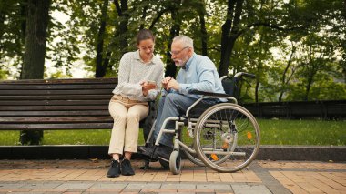 Genç bir kadın ve yaşlı bir adam parkta bankta oturmuş akıllı telefona bakıyor ve konuşuyorlar. Ortak ilgi ve bağlantı, nesiller arası boşlukları oluşturur.
